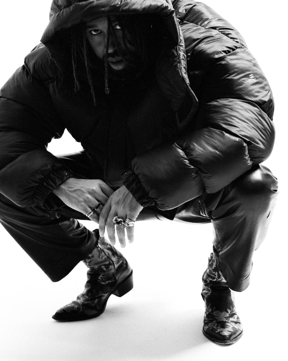 Puffer Jacket with the hood up in a seated studio portrait